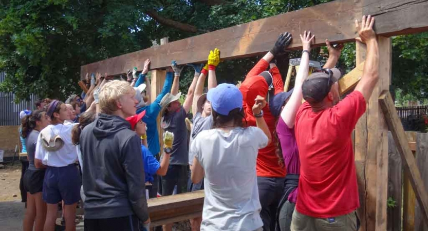 A group of people raise a long piece of wood during a service project. 